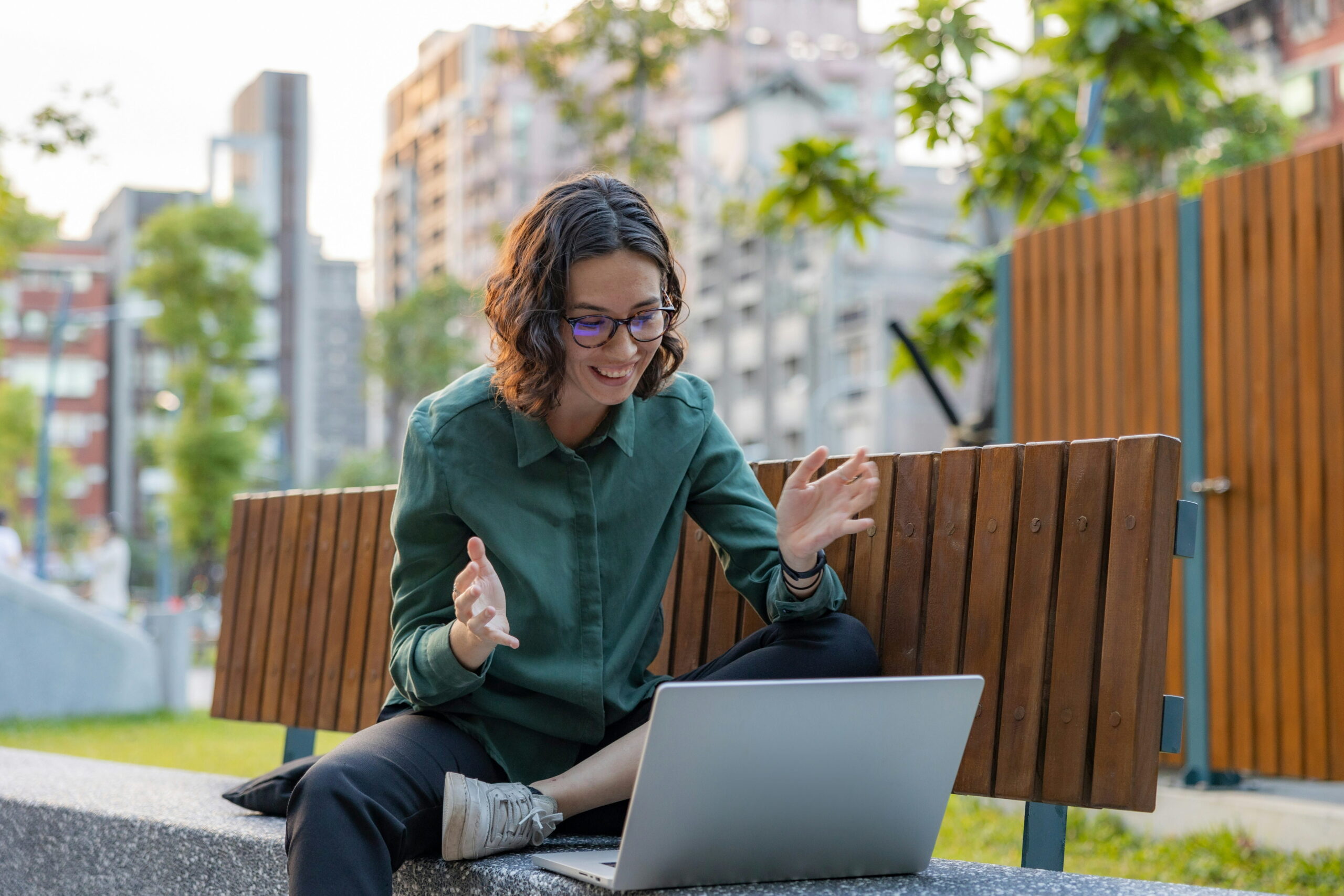 Femme souriante en rencontre de coaching en visioconférence, assise sur un banc de parc avec son ordinateur portable